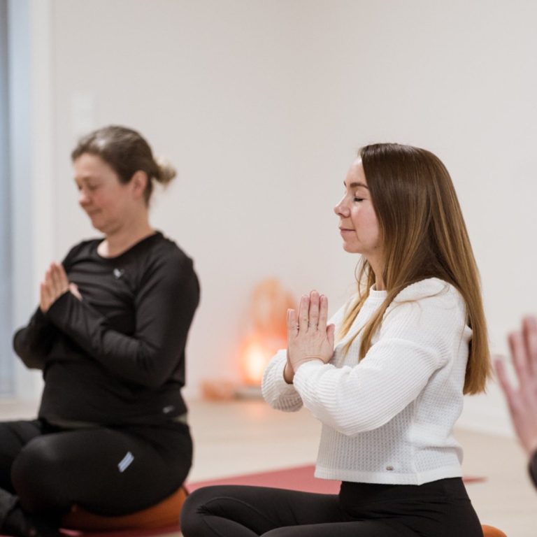 Yogakurse Zwei Frauen in entspannter Yoga-Pose mit gefalteten Händen, meditative Atmosphäre.